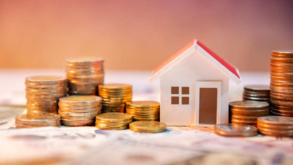 Coins stacked up next to a house model on a table.
